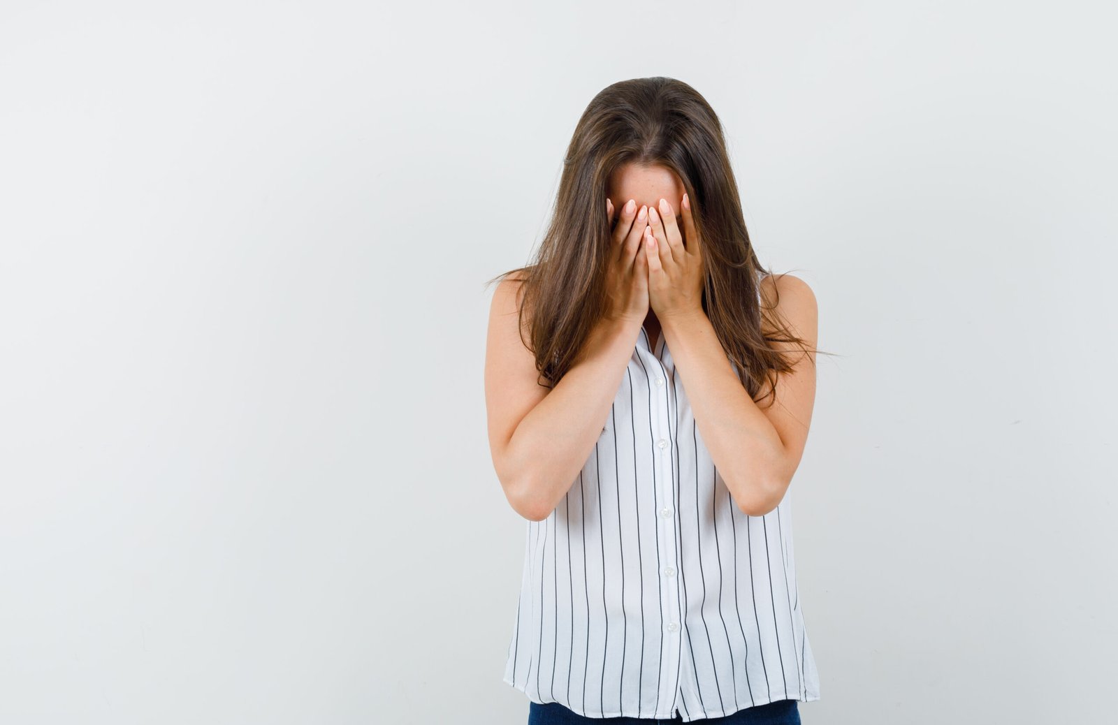 A young woman covering her face with her hands represents a lack of confidence and emotional exhaustion.