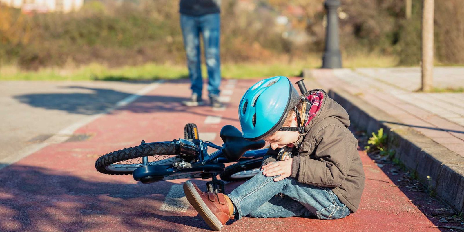 Boy sitting next to fallen bike holding arm wincing in pain