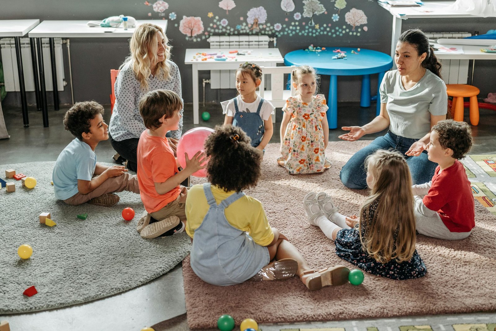 Kids and teachers sitting on a rug in a classroom talking