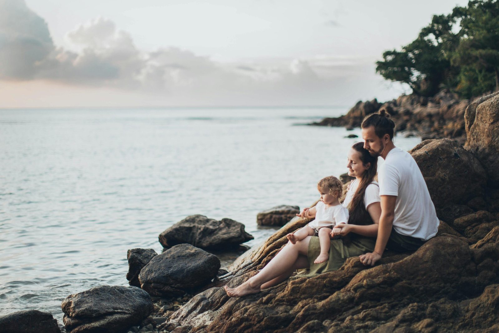 Mom, dad, and baby sitting on rocks looking out at the sea