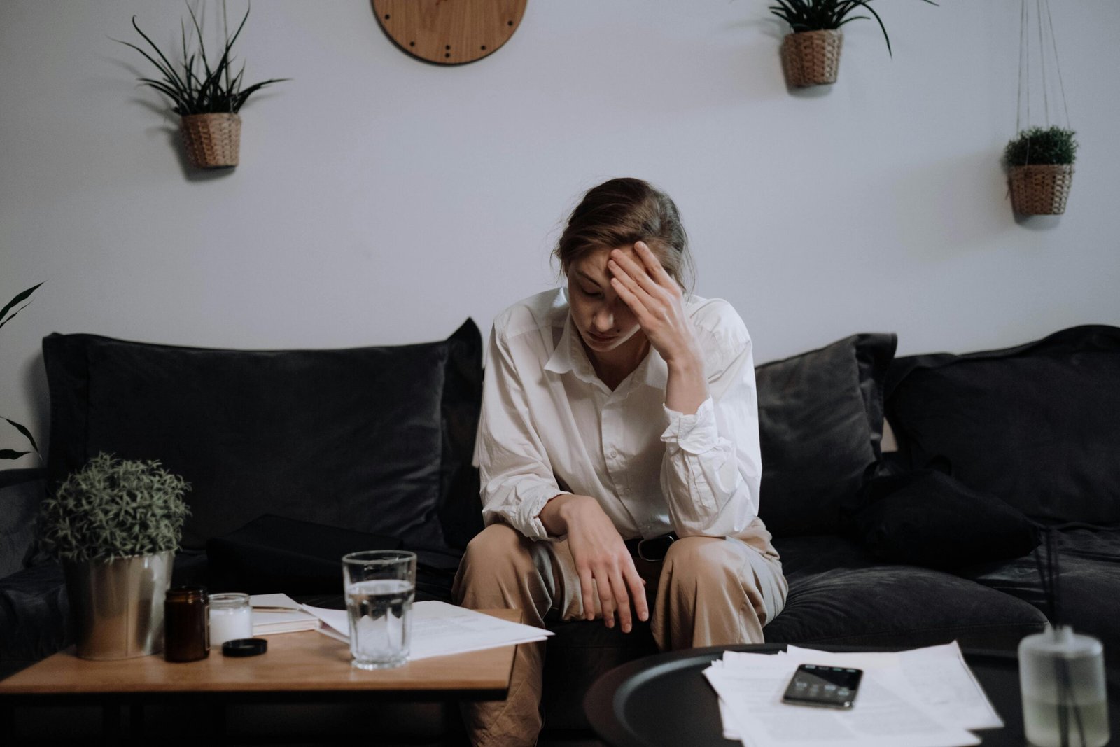 Stressed woman sitting on couch with books and work on the table in front of her.